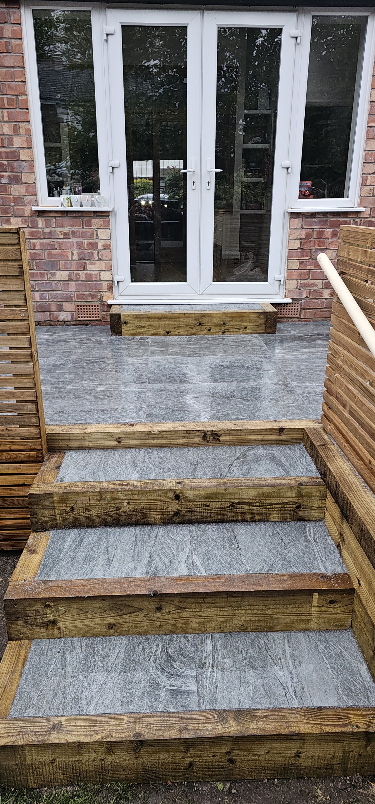 Grey porcelain patio with sleeper framed steps leading up to French doors